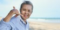 Asian senior woman sitting smiling and using hand sign is phone with talking on sea beach in summer holiday Royalty Free Stock Photo