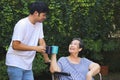 Asian senior woman sitting on wheelchair, drinking coffee or tea with her son in the garden. smiling happily Royalty Free Stock Photo