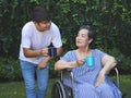 Asian senior woman sitting on wheelchair, drinking coffee or tea with her son in the garden. smiling happily Royalty Free Stock Photo