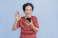 Asian senior woman smiles and video call isolated in grey background. Strong elderly grandmother feeling happy using mobile cell Royalty Free Stock Photo