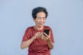 Asian senior woman smiles and video call isolated in grey background. Strong elderly grandmother feeling happy using mobile cell Royalty Free Stock Photo