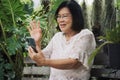 Asian senior woman using video calling on mobile smartphone relaxing at home garden. Leisure lifestyle relaxation solitude Royalty Free Stock Photo