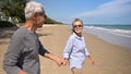 Asian senior woman wear sunglasses smile and holding hand husband walking running on beach in summer vacation