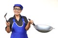 Asian senior woman, wears blue apron and cap, holds frying pan and spatula or ladle. Royalty Free Stock Photo