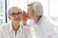 Asian senior woman holding hand near mouth telling funny,gossips on ears to friend,speaking in elderly woman ear and near face,