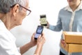 Asian senior woman receiving parcel post box from delivery service,paying deliver with smartphone to scan QR code payment purchase