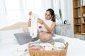 Asian single mother with big belly is about to give birth preparing clothes for her new baby. woman sits on the bed folding Royalty Free Stock Photo