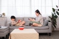 Asian single mother sitting on sofa relax using smartphone shopping online while handsome son laying down play game with tablet Royalty Free Stock Photo