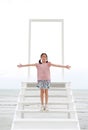 Asian smiling girl child arms wide open standing on open door gate with stairs to the sea and sky. Kid hands outstretched or