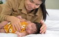 Smiling mother and child on white bed. Asian mom nursing her newborn baby girl at home Royalty Free Stock Photo