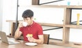 Asian smiling young man with casual  red t-shirt enjoy having breakfast, Young man cooking food and drink in the kitchen Royalty Free Stock Photo