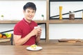 Asian smiling young man with casual red t-shirt enjoy having breakfast, eating sandwich, Young man cooking food in kitchen Royalty Free Stock Photo