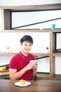 Asian smiling young man with casual  red t-shirt enjoy having breakfast, eating sandwich, Young man cooking food in kitchen Royalty Free Stock Photo