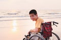 Asian special child on wheelchair on the sea beach with sunset on travel Royalty Free Stock Photo