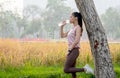 Asian sport woman lean tree and drink water from bottle with grass field as background during exercise in park or garden with Royalty Free Stock Photo