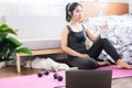 Asian sport woman relaxing and take a break after doing exercise hand holding bottle of water sitting on yoga mat with dumbbells