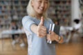 Asian student girl standing in library showing thumb up, closeup