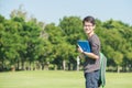 Asian student holding books and smiling while standing in park a Royalty Free Stock Photo
