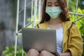Asian Student wear mask and typing report and research in garden. Business woman work on laptop.Young freelancer writing blog and Royalty Free Stock Photo