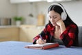 Asian student witgh headphone taking notes in the kitchen Royalty Free Stock Photo