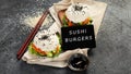 Asian sushi burger, soy sauce, chopstick on dark background. Trendy hybrid food