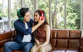 Asian sweet couple boyfriend, girlfriend sitting on sofa in cozy living room at home in morning, wearing headphones to listen Royalty Free Stock Photo