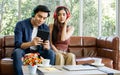 Asian sweet couple boyfriend, girlfriend sitting on sofa in cozy living room at home in morning, wearing headphones and using Royalty Free Stock Photo