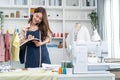 Asian tailor woman talking on phone with customer in tailoring atelier. Attractive beautiful young female fashion designer working Royalty Free Stock Photo