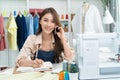 Asian tailor woman talking on phone with customer in tailoring atelier. Attractive beautiful young female fashion designer working Royalty Free Stock Photo