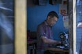 An Asian tailor work on the sewing machine, clothes hang on top.