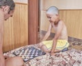 Asian tanned boy playing chess with an adult on the bed at home.