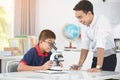 Asian teacher expanding to student in biology class with microscope .