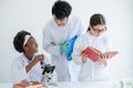 Asian teacher help and guide to African American young scientist child girl to analysis using microscope in laboratory or Royalty Free Stock Photo