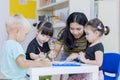 Asian teacher helps her students to paint on paper