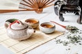 Asian teapot with teacups on bamboo tablamat decorated with chinese fan, lantern and scattered green tea on white marble Royalty Free Stock Photo