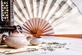 Asian teapot with teacups on bamboo tablamat decorated with chinese fan, lantern and scattered green tea on white marble Royalty Free Stock Photo