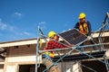 Asian technicians or workers wearing fall protection safety clothing carry solar cells to install on the roof of a house. Concept