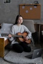 Asian teen girl playing guitar with laptop computer, learn to play with an online course in her room, sitting on the Royalty Free Stock Photo