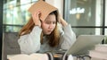 Asian teenage girl holding a book on her head stressed looking at laptop during online lessons from laptop