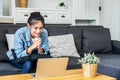 Asian teenage girl sitting on a sofa in the house is enjoying the work on the computer laptop, chatting through video conferencing Royalty Free Stock Photo