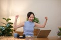 Asian teenage girl studying online on laptop, happy female student celebrating success sitting in living room at home. Royalty Free Stock Photo