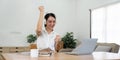 Asian teenage girl wearing headphones listening music while studying online on laptop, happy female student celebrating Royalty Free Stock Photo