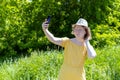 Asian teenage girl in yellow dress, hat and sunglasses takes selfie on phone, has video call, chats online in the park Royalty Free Stock Photo