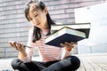 Asian teenage schoolgirl with a books and mobile phone in her hand,female student choosing between study and play,woman is
