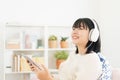 Asian teenager listening to music on tablet with headphone enjoy. Asia woman using computer happy smile while sitting on sofa at Royalty Free Stock Photo