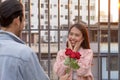 Asian teenager woman surprised and smiling at boyfriend gives red rose flowers at dinner in valentine day. young happy couple love Royalty Free Stock Photo