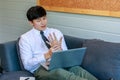 Asian tired overwork male businessman employee in business outfit sitting on sofa working with laptop computer holding hand