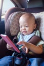 Asian toddler baby boy sitting in car seat and watching a video from smart phone