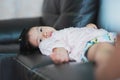 Asian toddler girl laying down on dark brown sofa with sad eyes. Adorable kid sleepy with unhappy face. Royalty Free Stock Photo