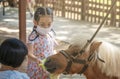 Asian tourist child girl is feeding the pony in zoo of Thailand, wearing medical or protective mask and feeding vegetable to pony Royalty Free Stock Photo